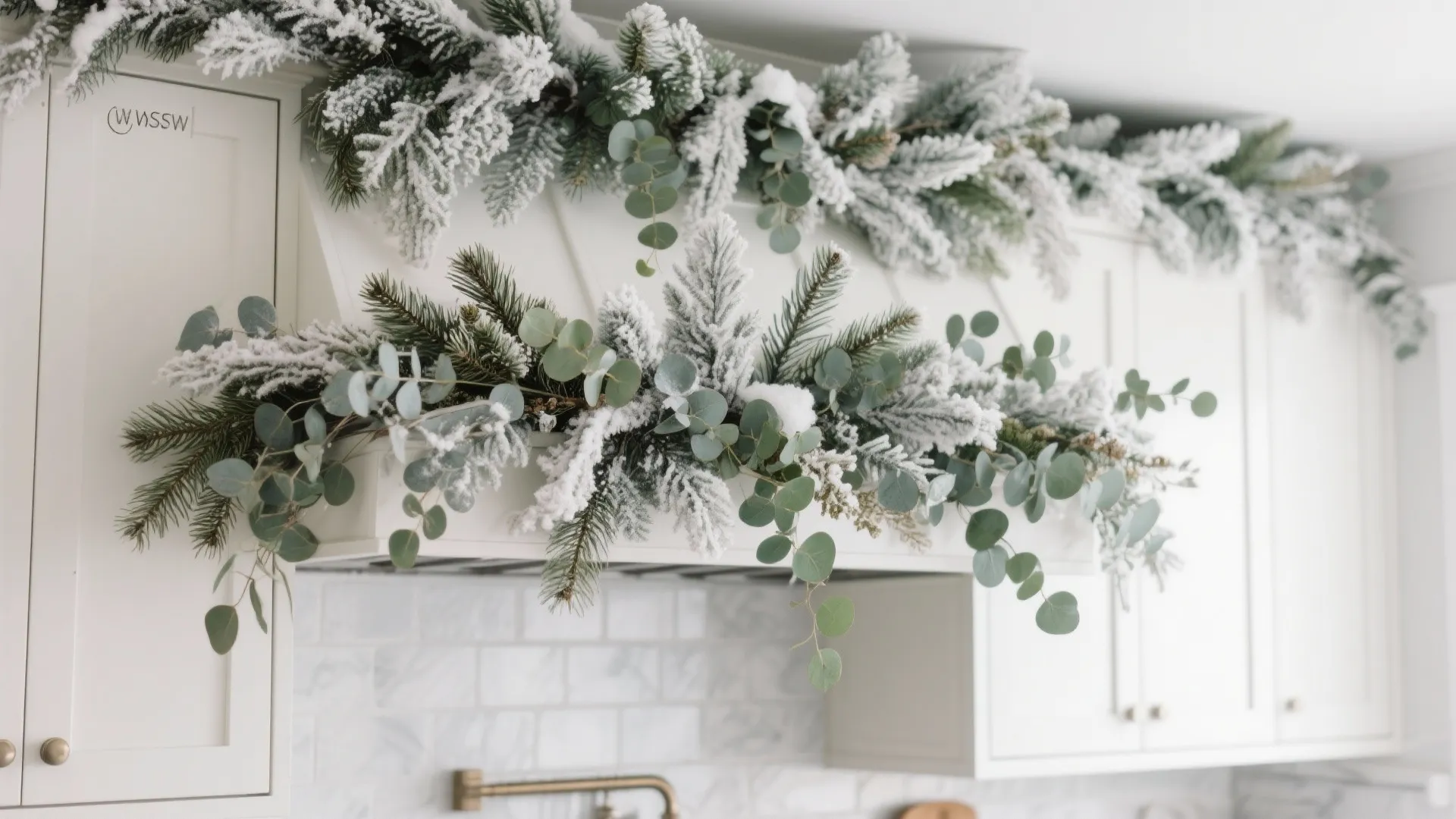 Snowy faux greenery layered above kitchen cabinets