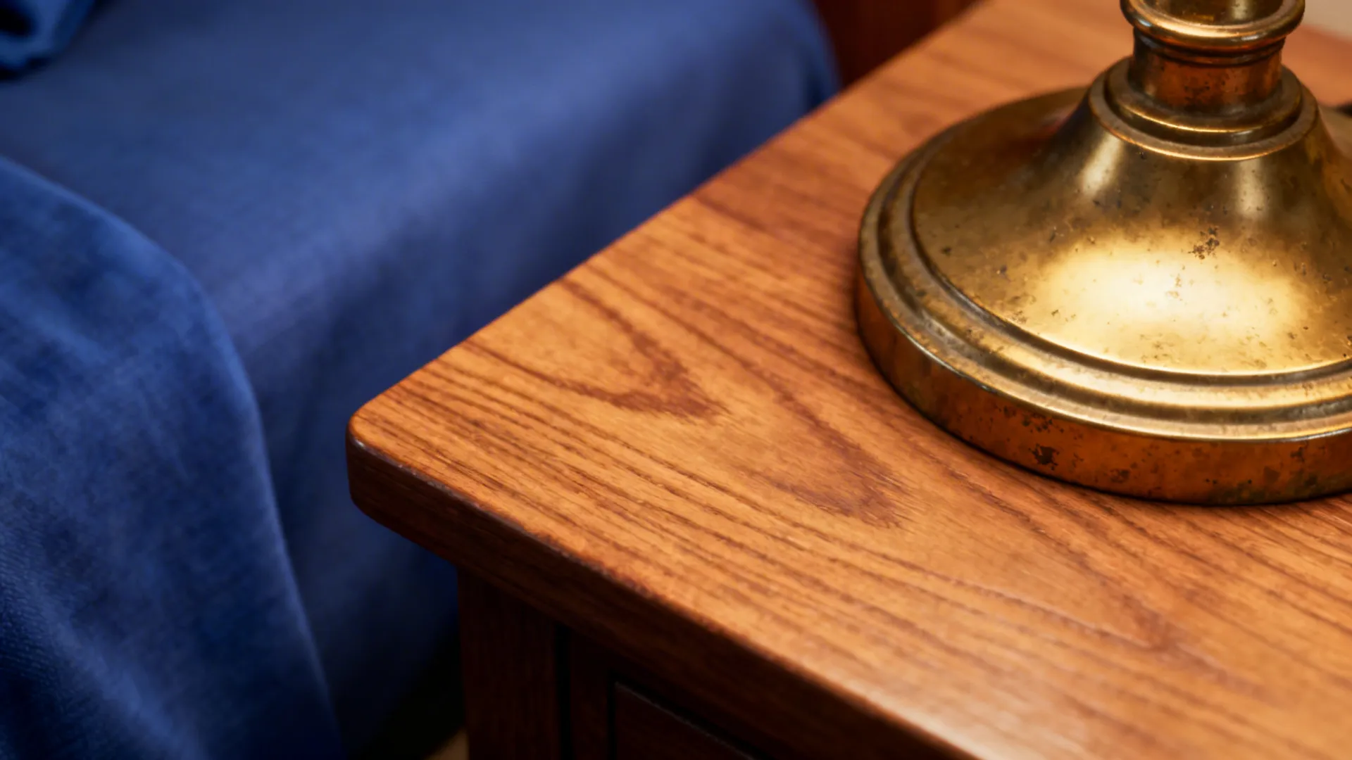 Close-up of oak table edge and brass lamp base next to royal blue fabric