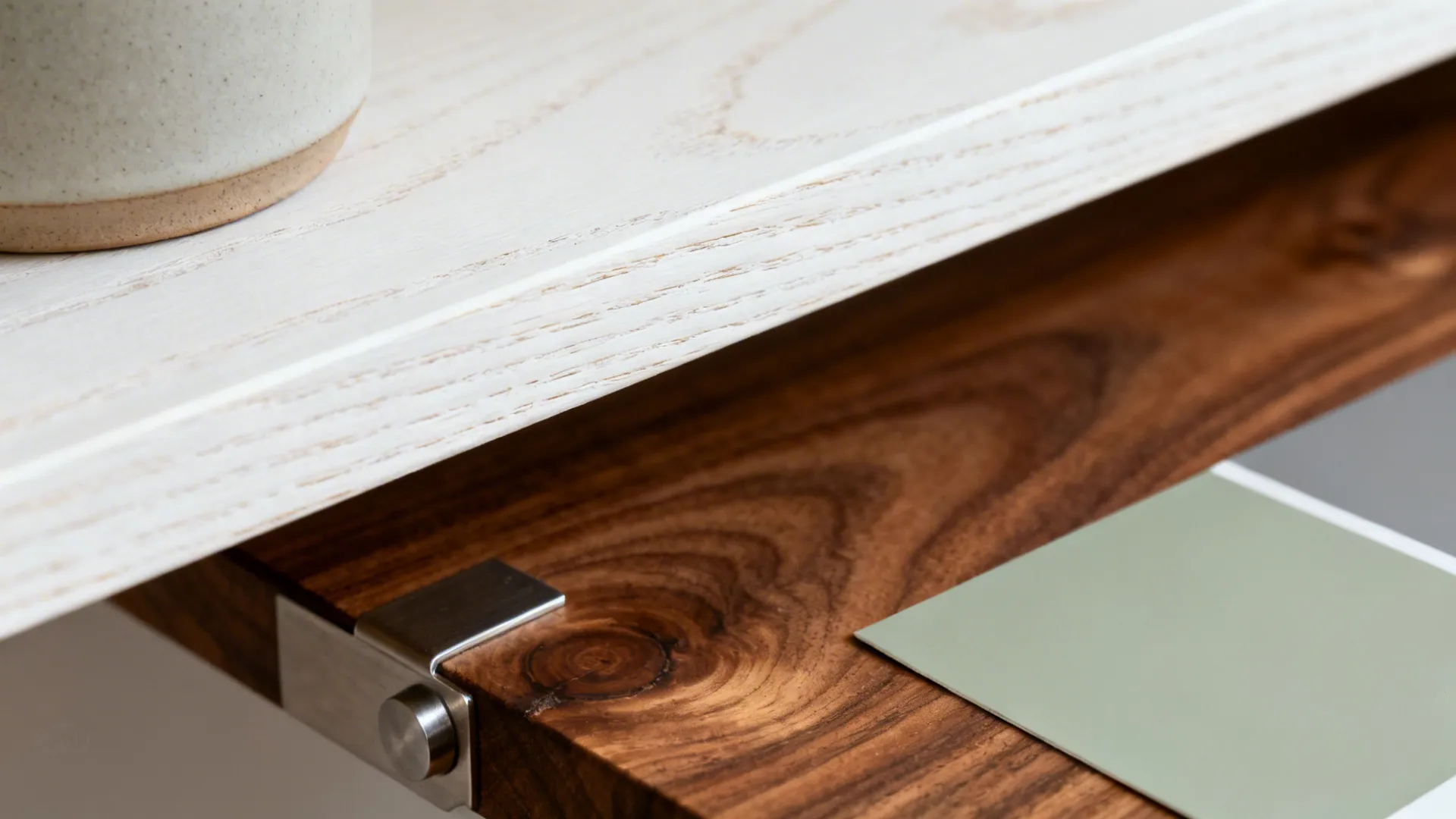 Macro of white oak and walnut grains with a muted sage paint swatch under soft daylight.