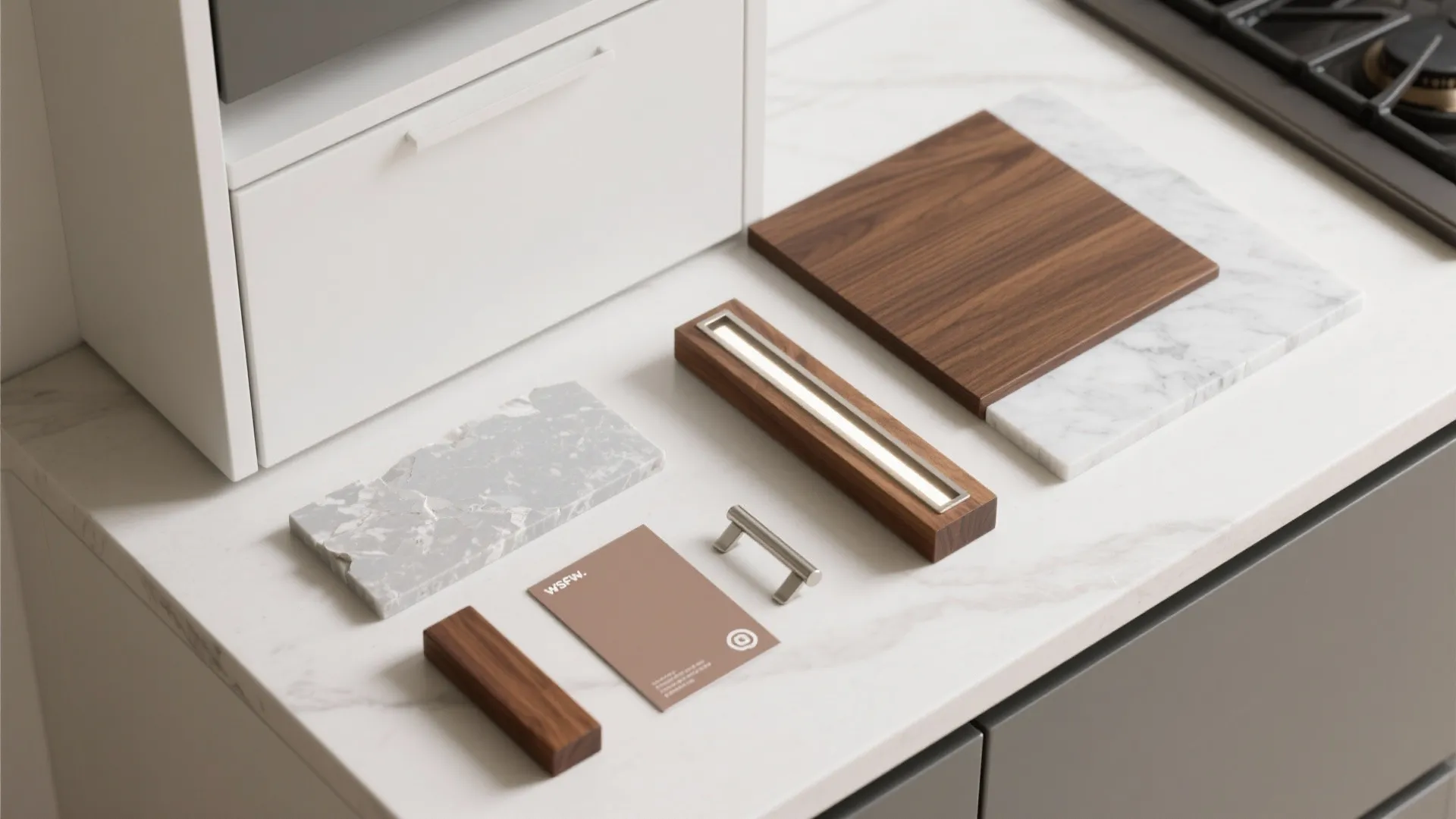 Material samples including wood blocks marble tiles and metal handles placed on white kitchen counter surface
