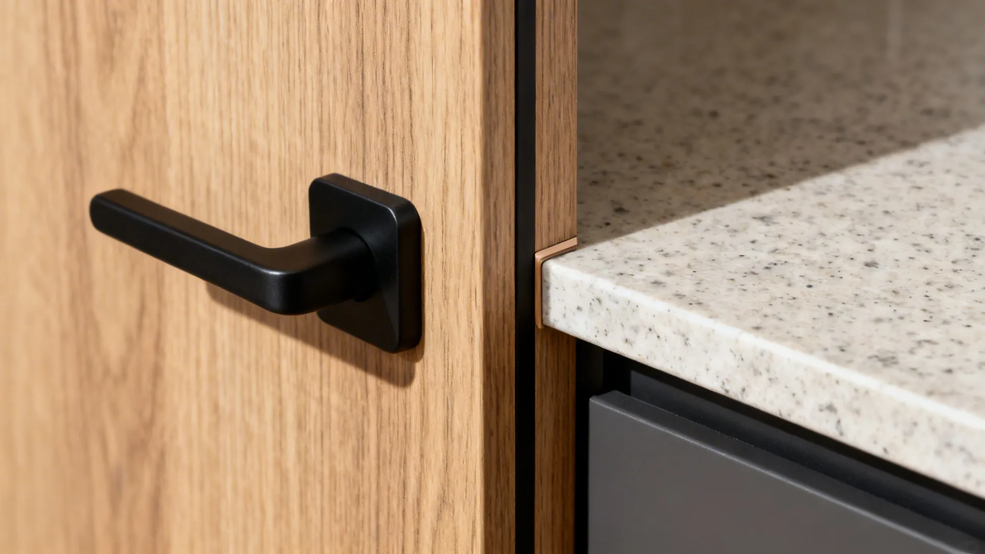 Black handle on light wood door next to a speckled stone kitchen countertop surface detail