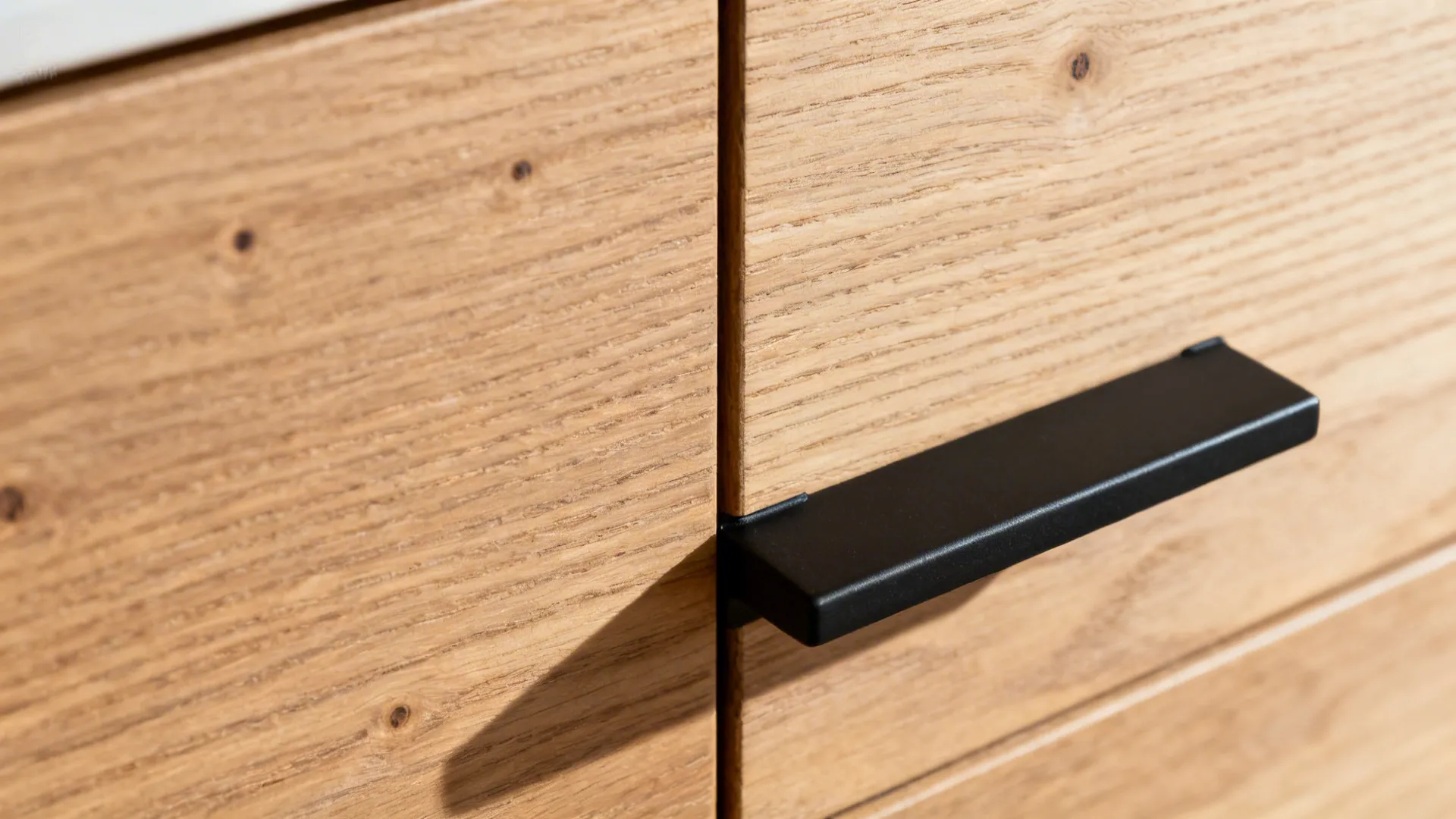 Macro of rift-cut oak cabinet grain with a matte black pull under warm light.