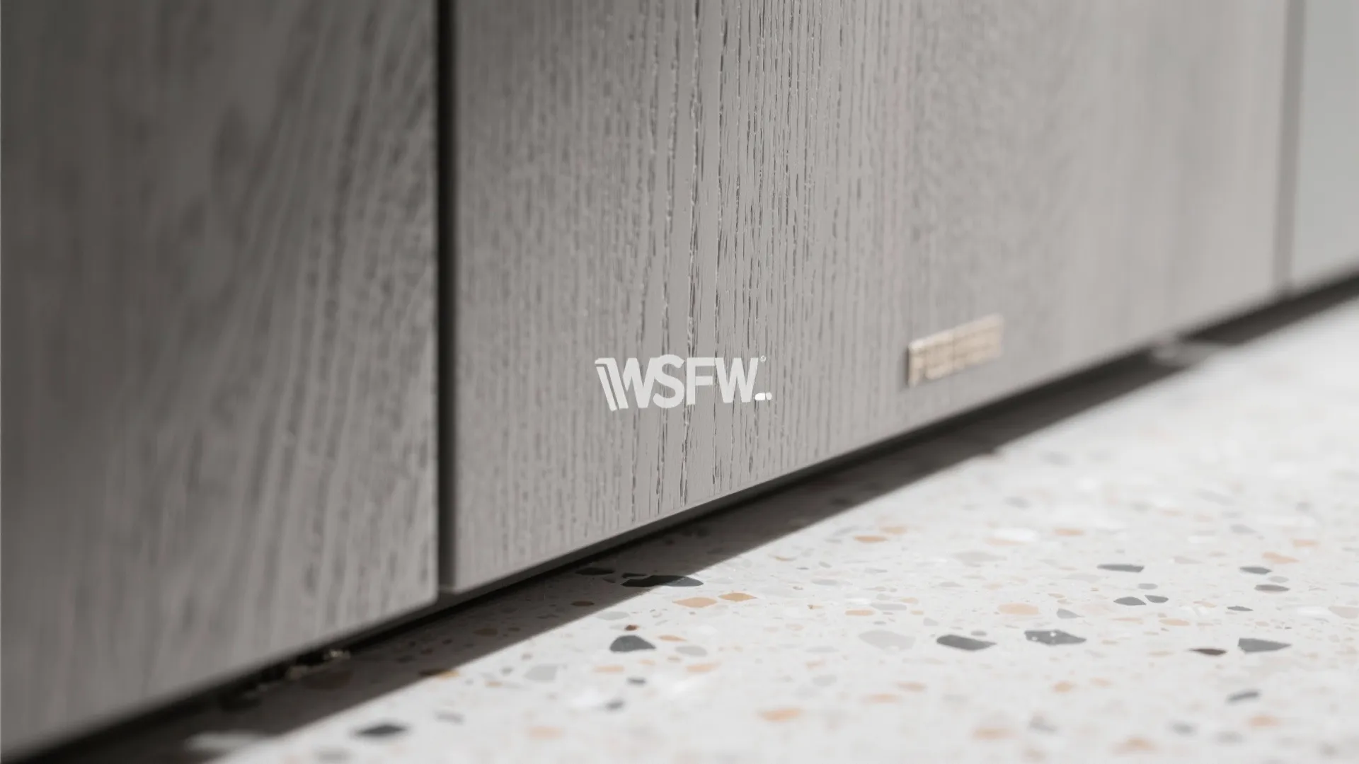 Close up view of grey wood kitchen cabinet doors with textured surface over terrazzo flooring