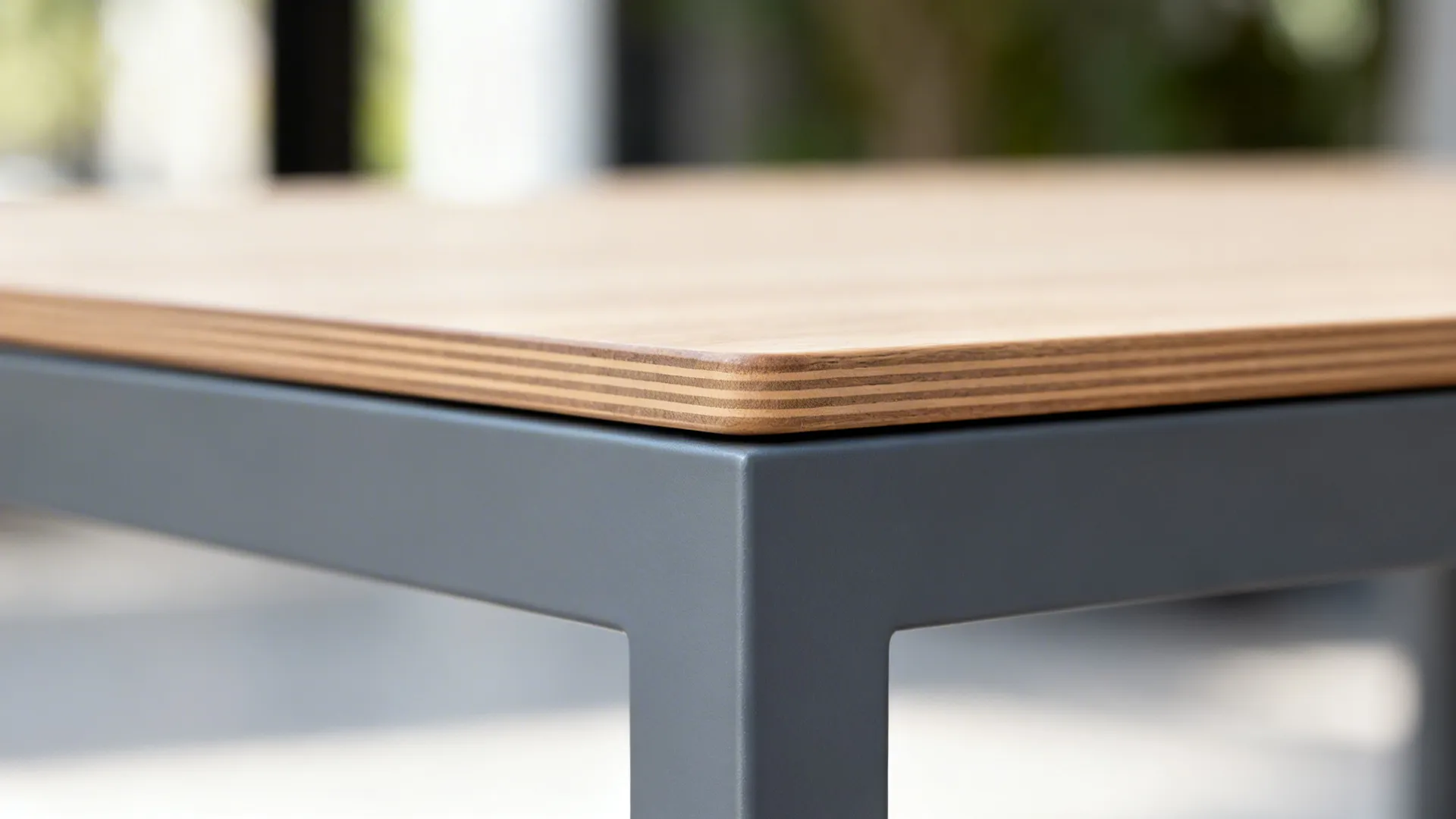 Close-up of a slim wood tabletop meeting a matte black steel leg with clean joinery.
