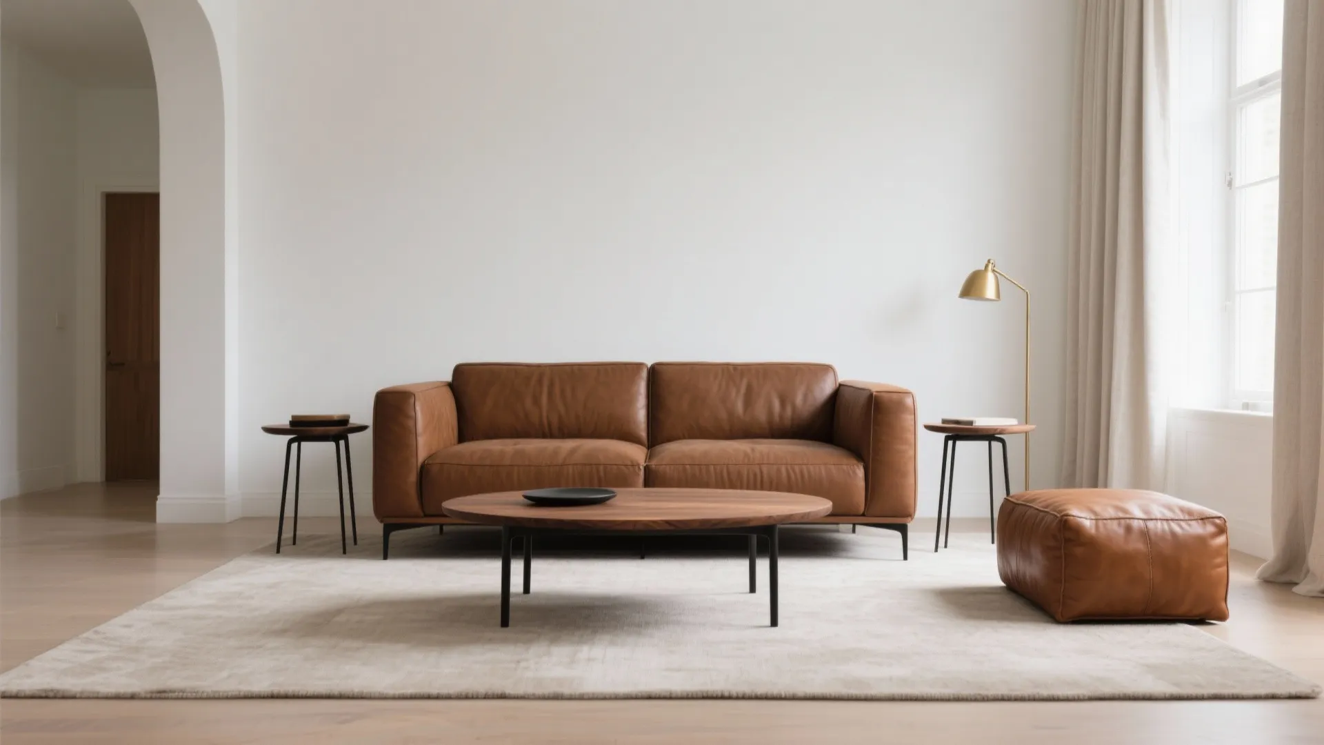Minimalist living room showing brown leather sofa wooden coffee table gold floor lamp and leather footrest