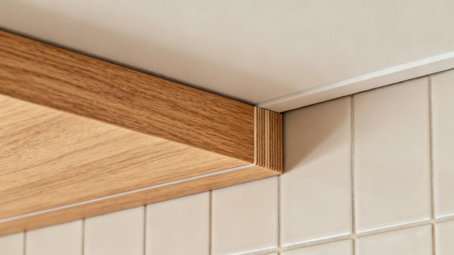 Macro of oak-look floating shelf meeting tile backsplash and POP ceiling edge.