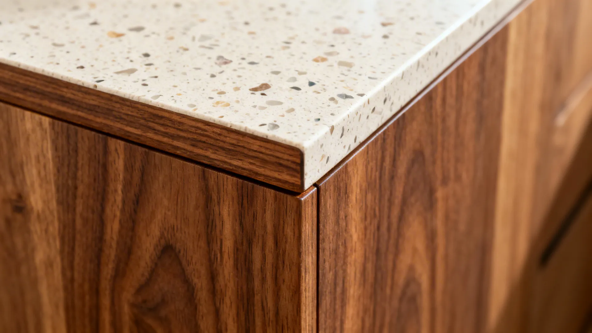Macro of rift-cut walnut edge meeting a pale terrazzo countertop.
