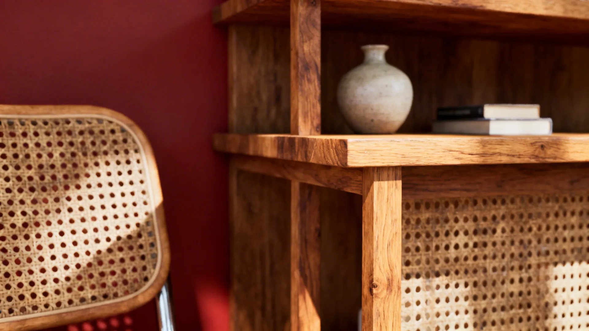 Oak shelves and rattan chair textures against a red accent wall, highlighting warm natural materials.