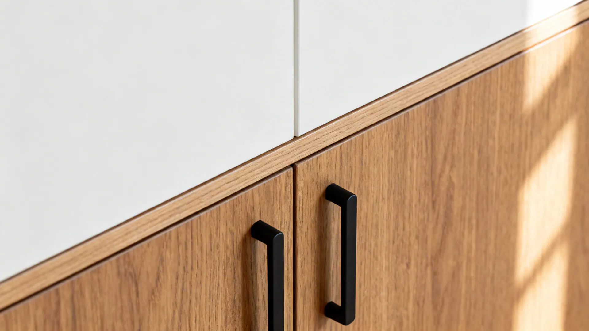 Macro of oak veneer meeting matte white panel with aligned black handles.