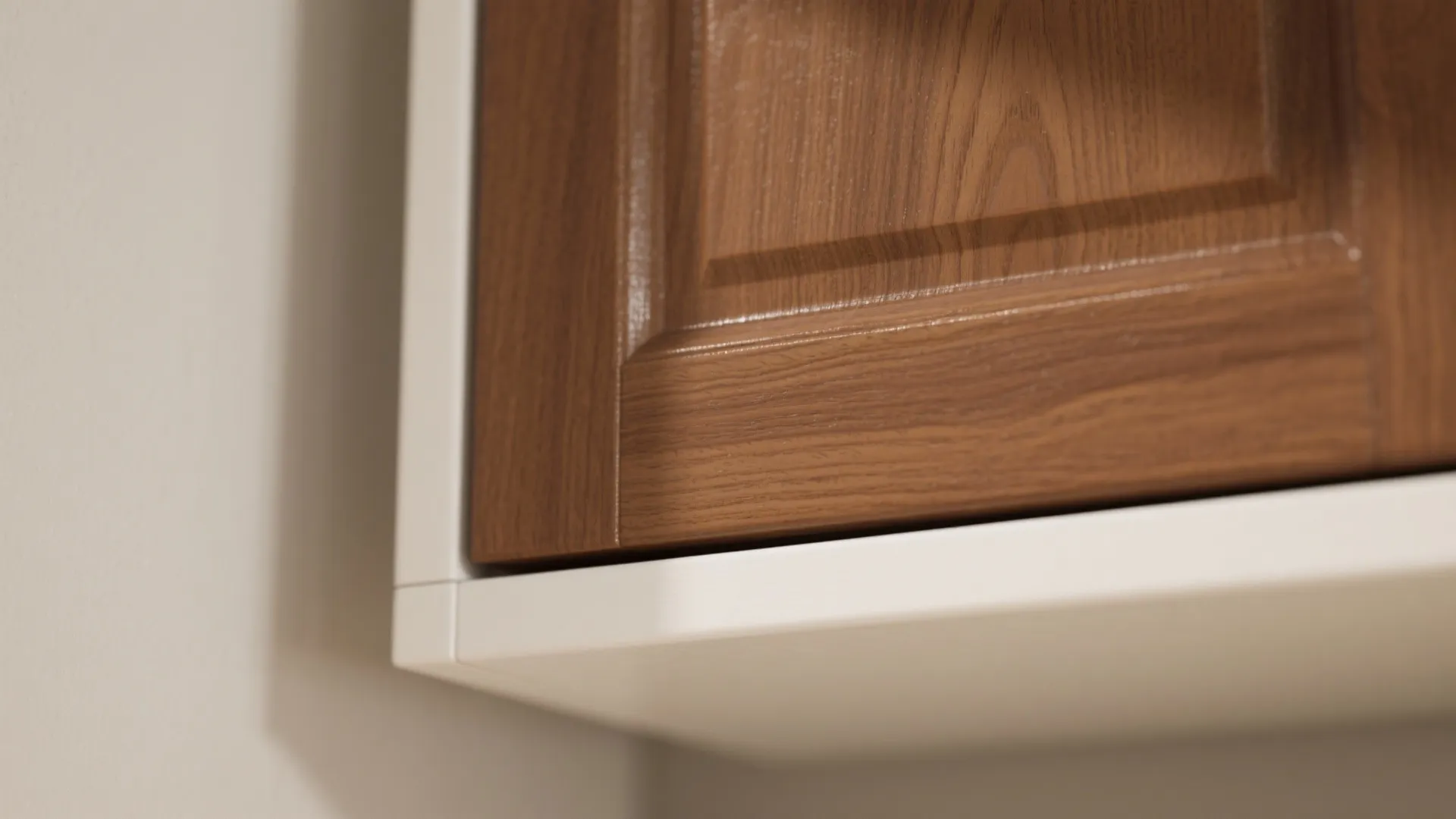 Close up of brown wood cabinet door with visible grain meeting a white kitchen cabinet frame