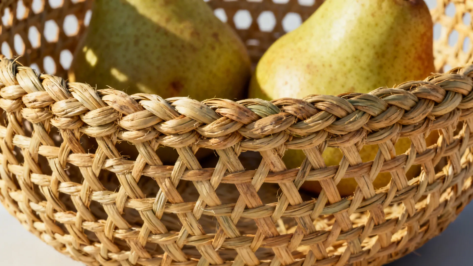 Macro of a seagrass fruit bowl with tight knots and breathable weave around a pear.