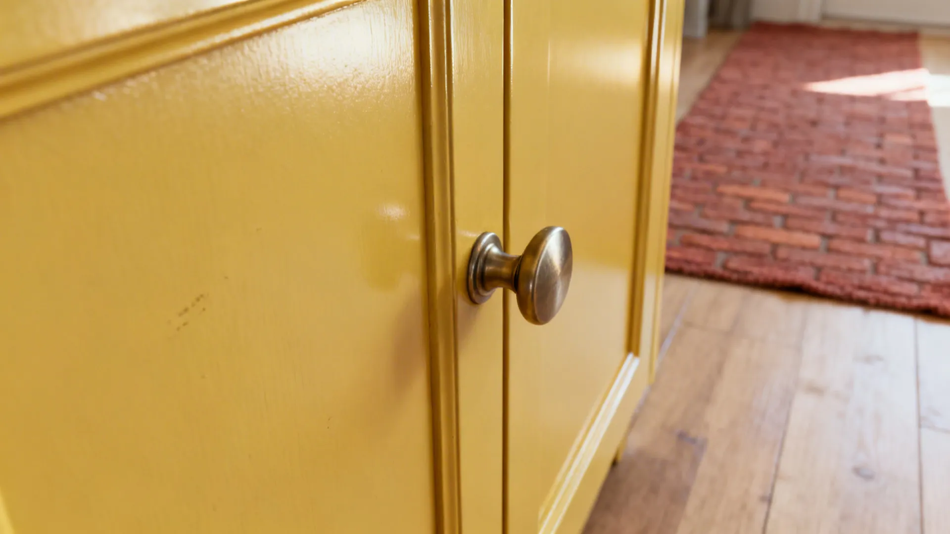 Macro of satin yellow cabinet door with brushed pull and soft red runner blurred behind.
