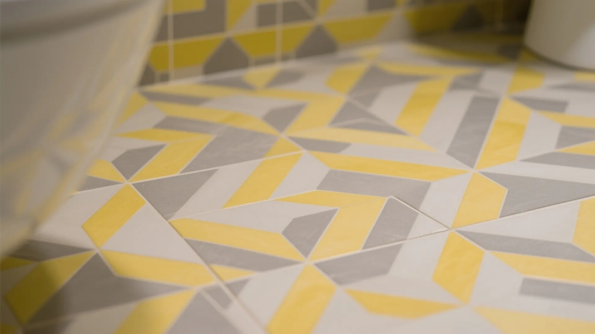 Close up of bathroom floor tiles featuring a geometric pattern in yellow grey and white