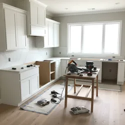 Unfinished kitchen during remodel with white cabinets marble wall large windows and tools on wooden table