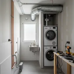 Laundry room under renovation with stacked washing machines, small wall sink, window, and exposed pipes