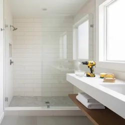 Modern white bathroom with glass shower door wall tiles and yellow power drill cleaning tool