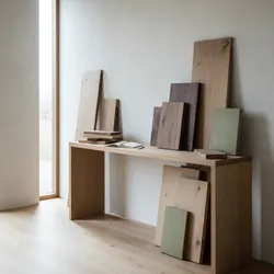 Wooden console table against white wall showing various wood planks and samples in a bright room