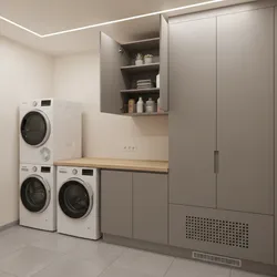 Modern laundry room with white washing machines, dryer, grey wall cabinets, and light wooden countertop