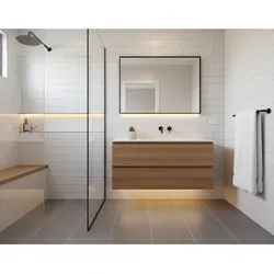 Modern bathroom with wood cabinet, rectangular mirror, white wall tiles, glass shower, and gray floor
